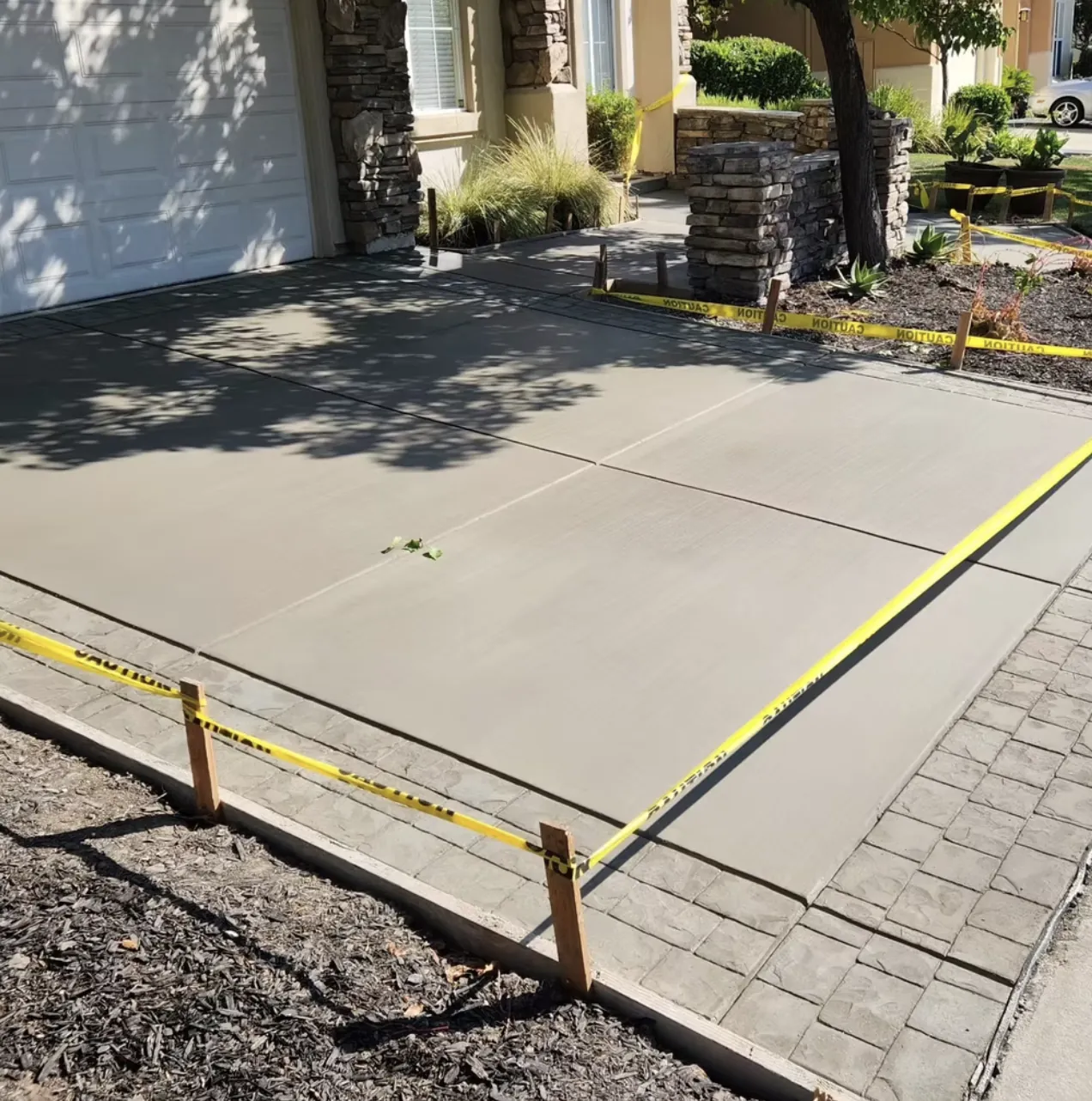 Freshly finished concrete driveway apron with survey tape and stakes beside a stamped concrete border