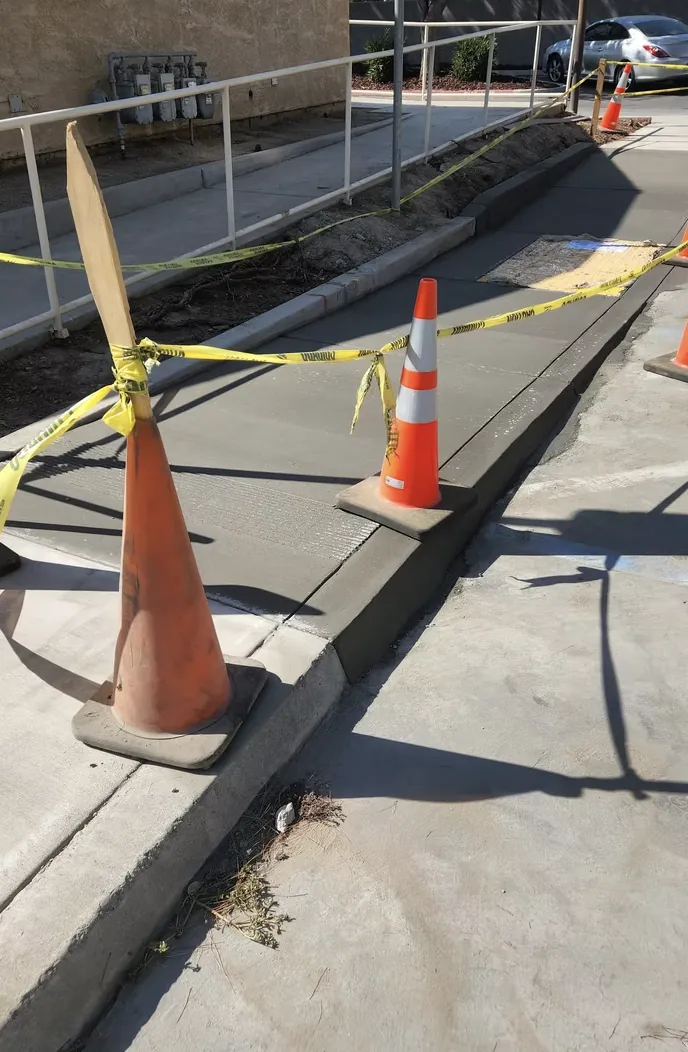 Newly poured concrete sidewalk with a smooth broom finish and safety cones on the curb
